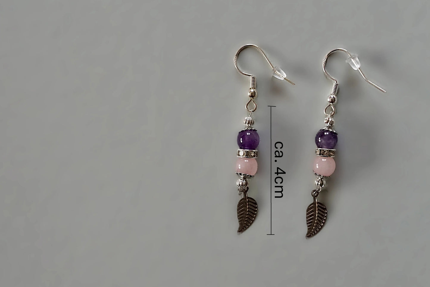 Ohrringe mit silberfarbenen Haken, zwei Edelsteinperlen in Amethyst und Rosenquarz sowie einem silberfarbenen Blattanhänger mit Maßstab