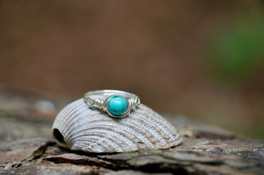 Ring mit einer Turquenit Edelsteinperle eingefasst in versilbertem Kupferdraht, platziert auf einer Muschel