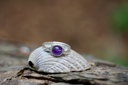 Ring mit einer Amethyst Edelsteinperle eingefasst in versilbertem Kupferdraht, platziert auf einer Muschel