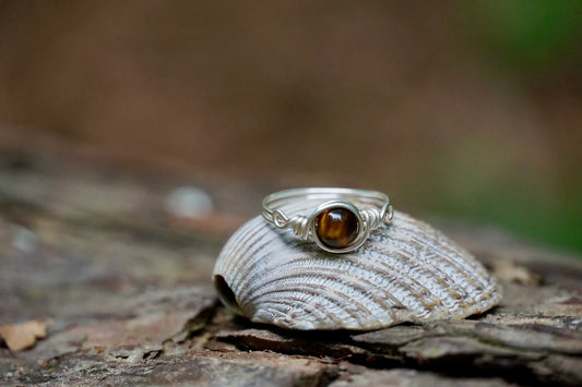 Ring mit versilbertem Kupferdraht und einer Edelstein Tigeraugeperle in der Mitte auf einer Muschel
