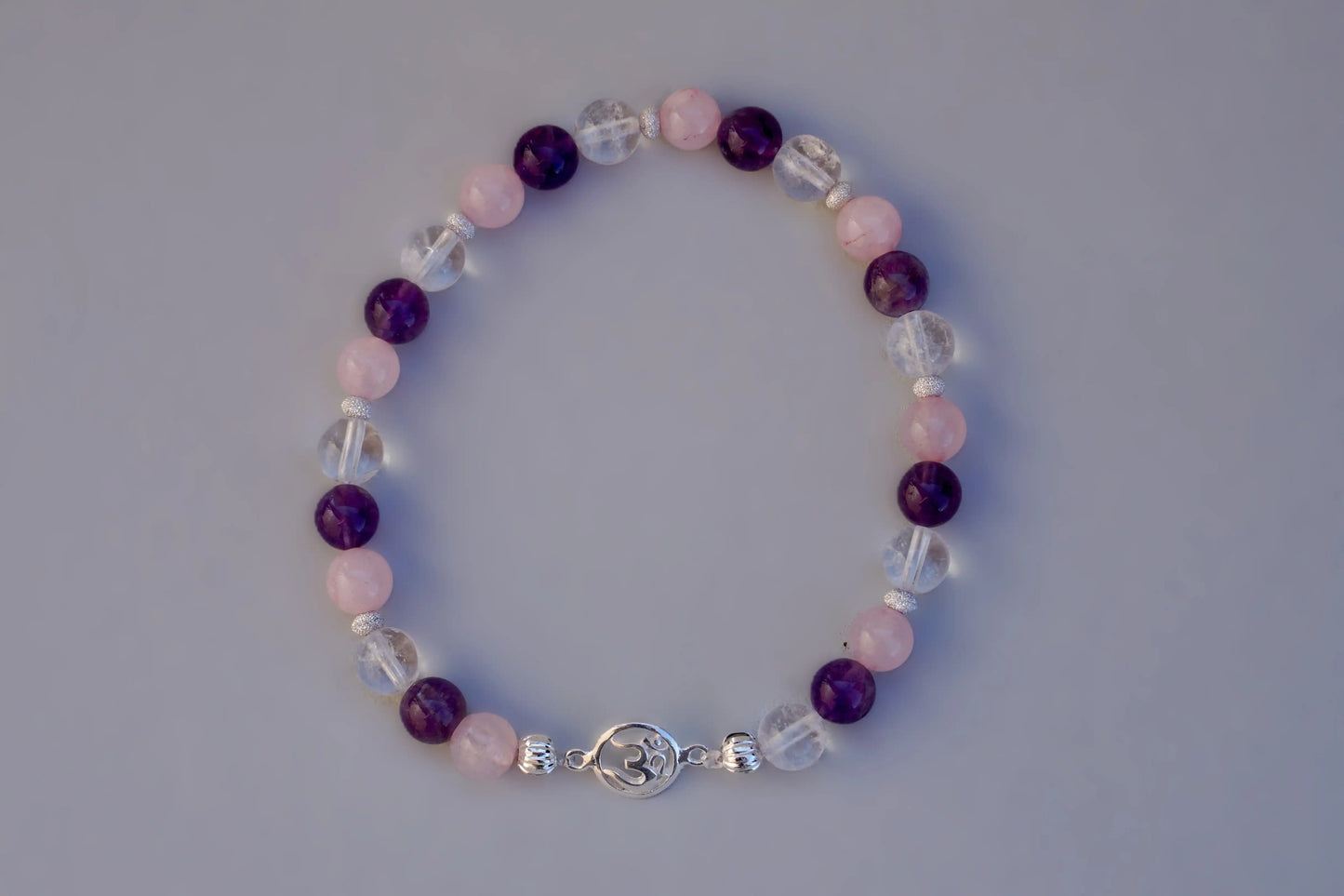 Rundes Armband aus Rosenquarz, Amethyst und Bergkristall mit silbernem Om-Anhänger und kleinen Silberperlen