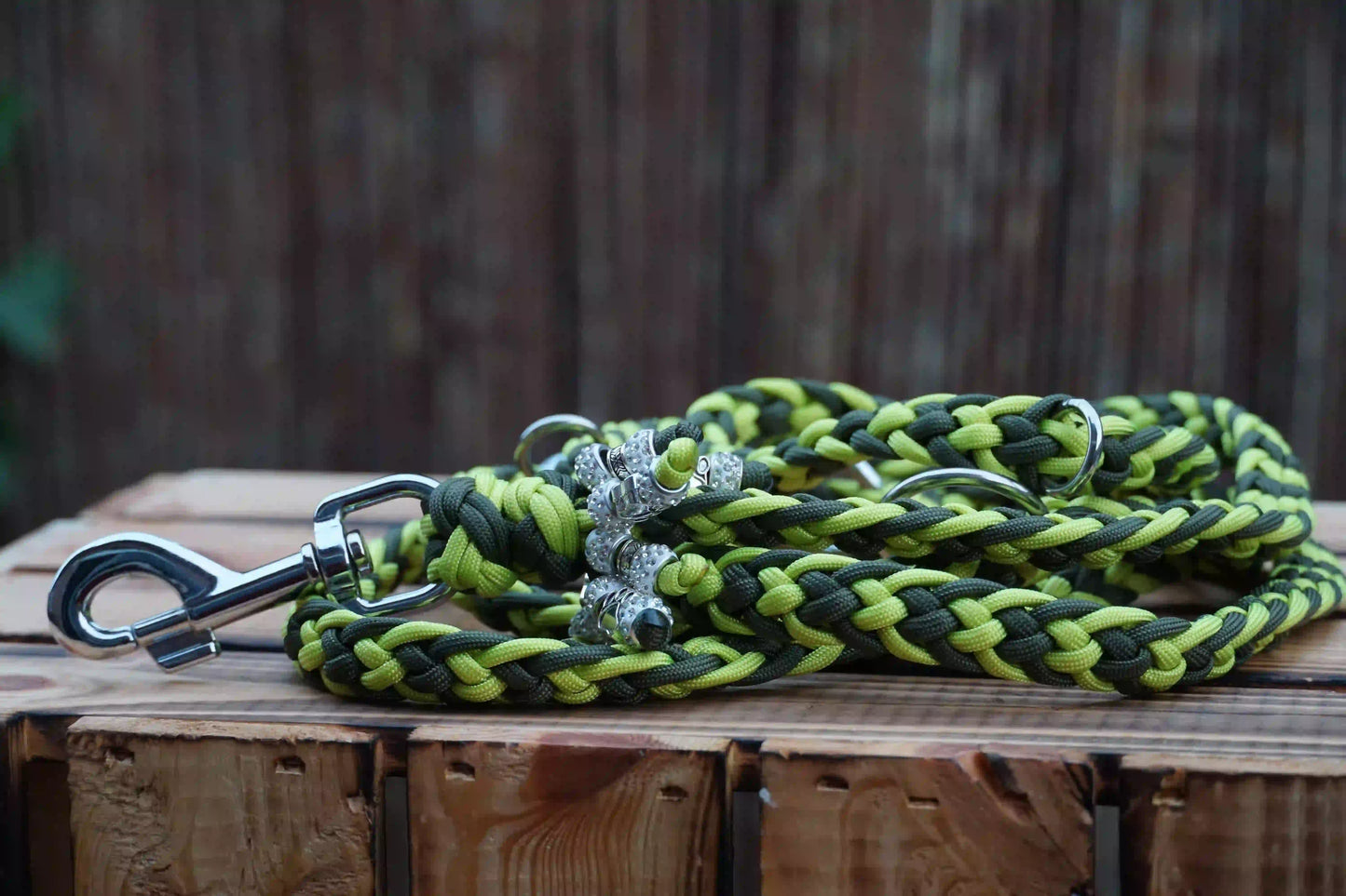 Geflochtene Hundeleine aus Paracord in Limettengrün und Olivgrün mit Metallkarabiner und zwei silbernen anhängern auf Holztisch