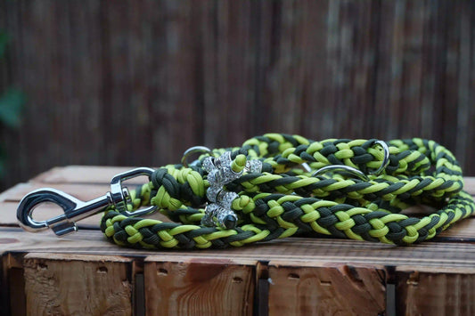 Geflochtene Hundeleine aus Paracord in Limettengrün und Olivgrün mit Metallkarabiner und zwei silbernen anhängern auf Holztisch