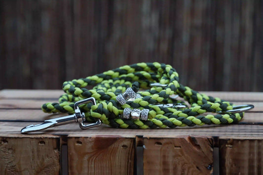 Geflochtene Hundeleine aus Paracord in Limettengrün und Olivgrün mit Metallclip und Schmuckperlen auf Holztisch.