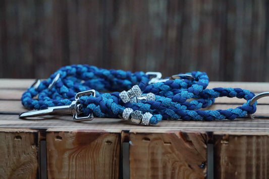 Marineblaue, schmale Hundeleine aus Paracord mit reflektierenden blauen Akzenten und Metallringen, liegend auf Holz.