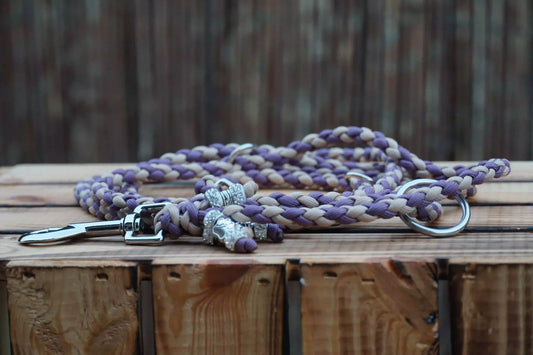 Schmale Hundeleine aus geflochtenem Paracord in den Farben Mauve und Mocca mit Metallkarabiner und Ring auf Holztisch