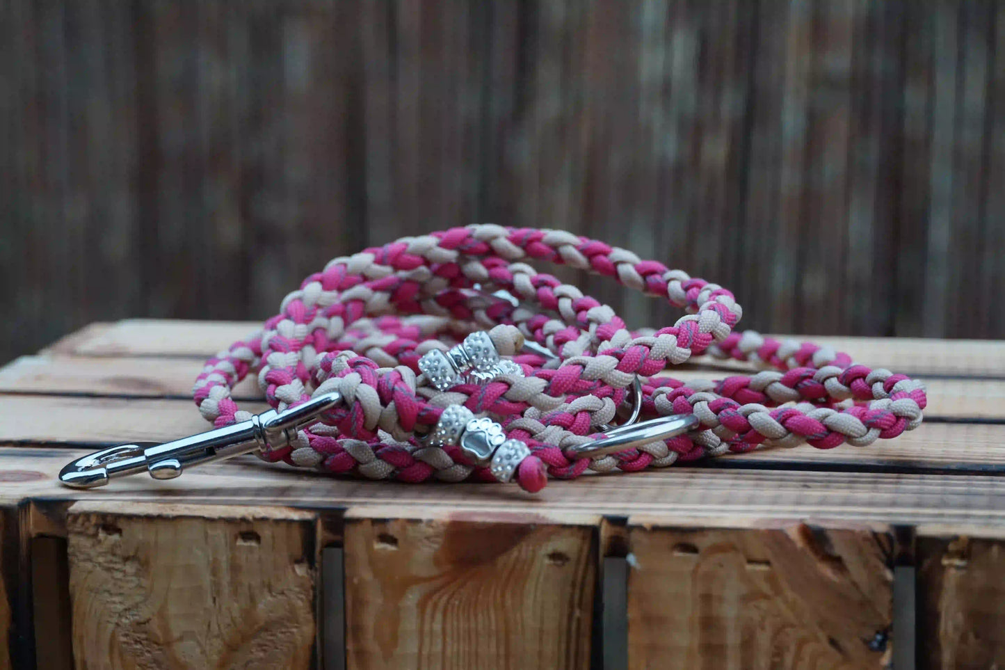 Schmale Hundeleine aus Paracord in Mocca und reflektierendem Pink mit Metallkarabinern auf Holzkiste.