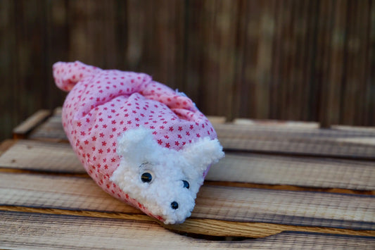 Kuscheltier in Form eines weißen Hasenkopfes mit Knopfaugen, eingewickelt in rosa Stoff mit Sternen auf Holztisch