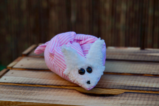 Kuscheltier in Form eines weißen Hasenkopfes mit Knopfaugen, eingewickelt in rosa weiß gestreiften Stoff, auf Holztisch