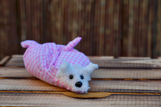 Kuscheltier in Form eines weißen Hasenkopfes mit Knopfaugen, eingewickelt in rosa-weiß karierten Stoff, auf Holztisch