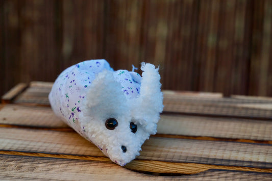 Kuscheltier in Form eines weißen Hasenkopfes mit Knopfaugen, eingewickelt weißem Blümchen Stoff auf Holztisch