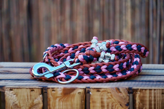 Geflochtene Paracord Hundeleine in Bronze, rosa und Anthrazittönen mit Metallkarabiner und Schmuckperlen am Griff auf holzkiste