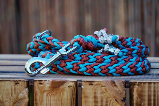 Geflochtene Paracord Hundeleine in Bronze- und Blautönen mit Metallkarabiner und Schmuckperlen am Griff auf Holzkiste