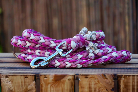 Geflochtene Paracord Hundeleine in Rosa- und Weißtönen mit Metallkarabiner und Schmuckperlen am Griff auf holzkiste