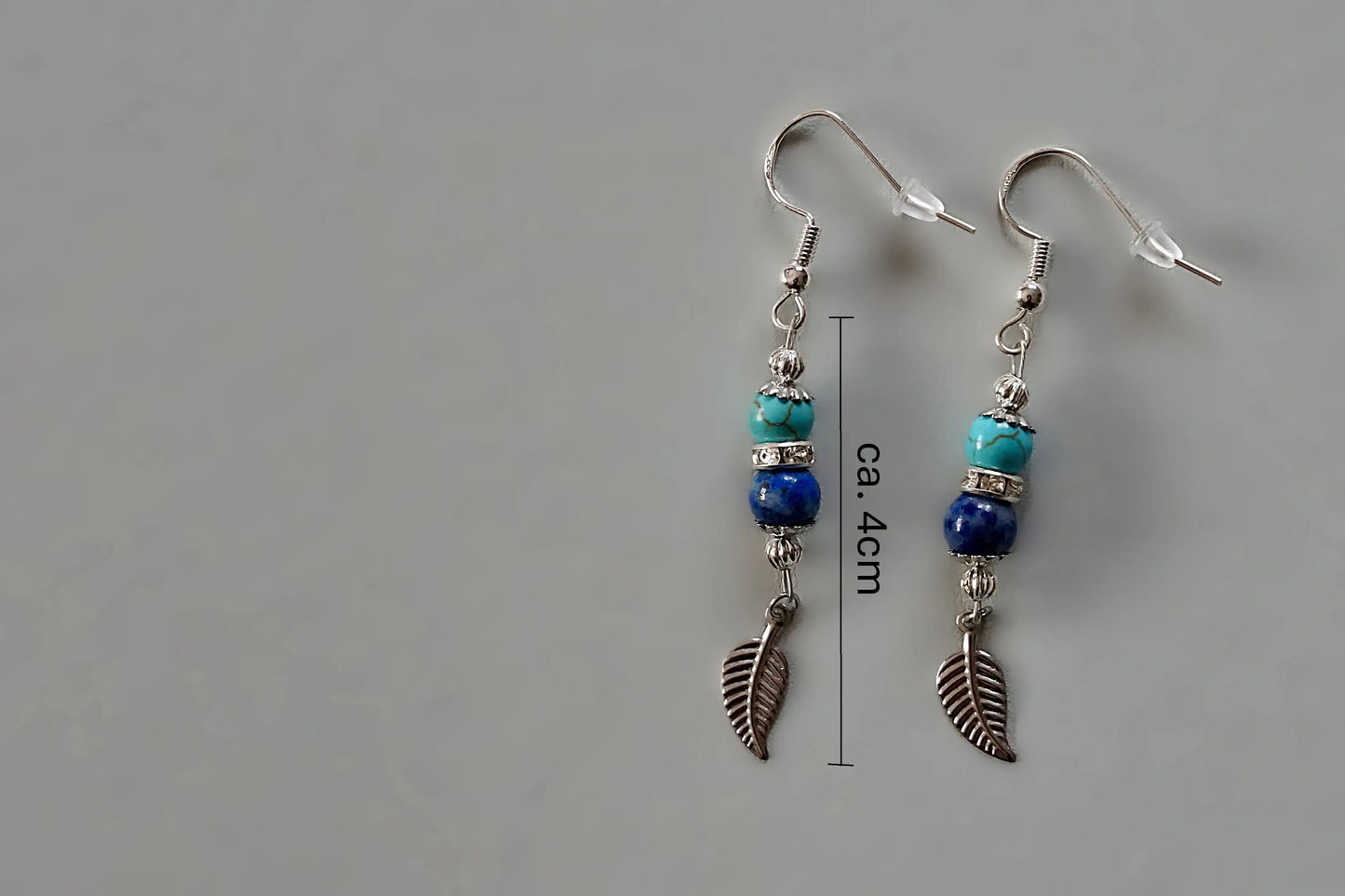 Ohrringe mit silberfarbenen Haken, zwei Edelsteinperlen in Turquenit und Sodalith sowie einem silberfarbenen Blattanhänger mit Maßstab