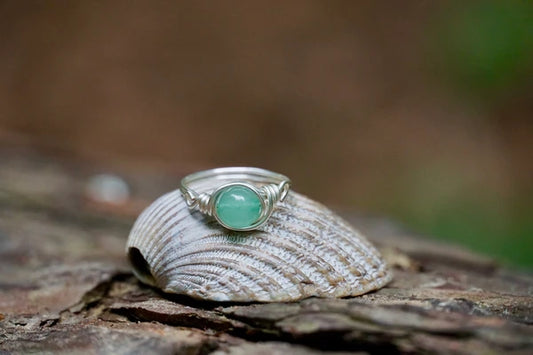 Ring mit einer grünen Aventurin Edelsteinperle eingefasst in versilbertem Kupferdraht, platziert auf einer Muschel