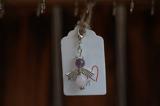 Anhänger in Form eines Schutzengels mit Amethyst- und Rosenquarzperlen, silberfarbene Flügel, an einem Band befestigt.