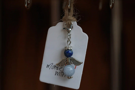 Anhänger in Form eines Schutzengels mit Sodalith- und Chalcedonperlen, silberfarbene Flügel, an einem Band befestigt.