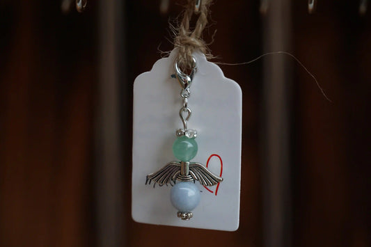 Anhänger in Form eines Schutzengels mit grüner Aventurin- und Chalcedonperlen, silberfarbene Flügel, an einem Band befestigt.