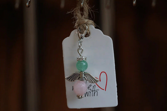 Anhänger in Form eines Schutzengels mit grüner Aventurin- und Rosenquarzperlen, silberfarbene Flügel, an einem Band befestigt.