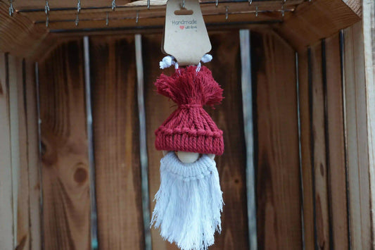 Burgunder gestrickte Mütze mit Bommel auf einer Holzfigur mit weißem, langem Bart, hängend vor Holzlatten.