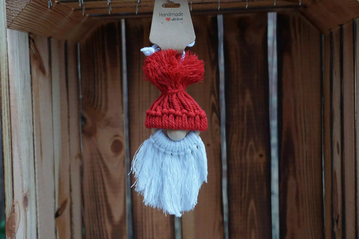 Rote gestrickte Mütze mit Bommel auf einer Holzfigur mit weißem, langem Bart, hängend vor Holzlatten.