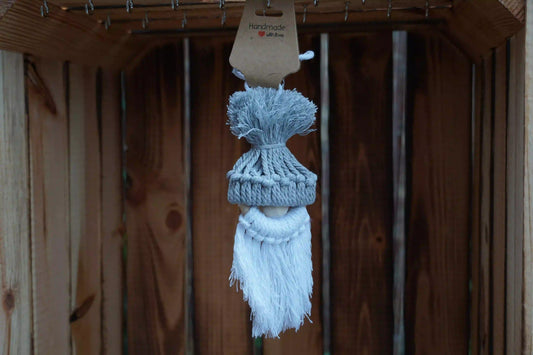 graue gestrickte Mütze mit Bommel auf einer Holzfigur mit weißem, langem Bart, hängend vor Holzlatten.