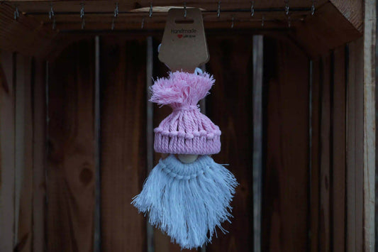 Rosa gestrickte Mütze mit Bommel auf einer Holzfigur mit weißem, langem Bart, hängend vor Holzlatten.