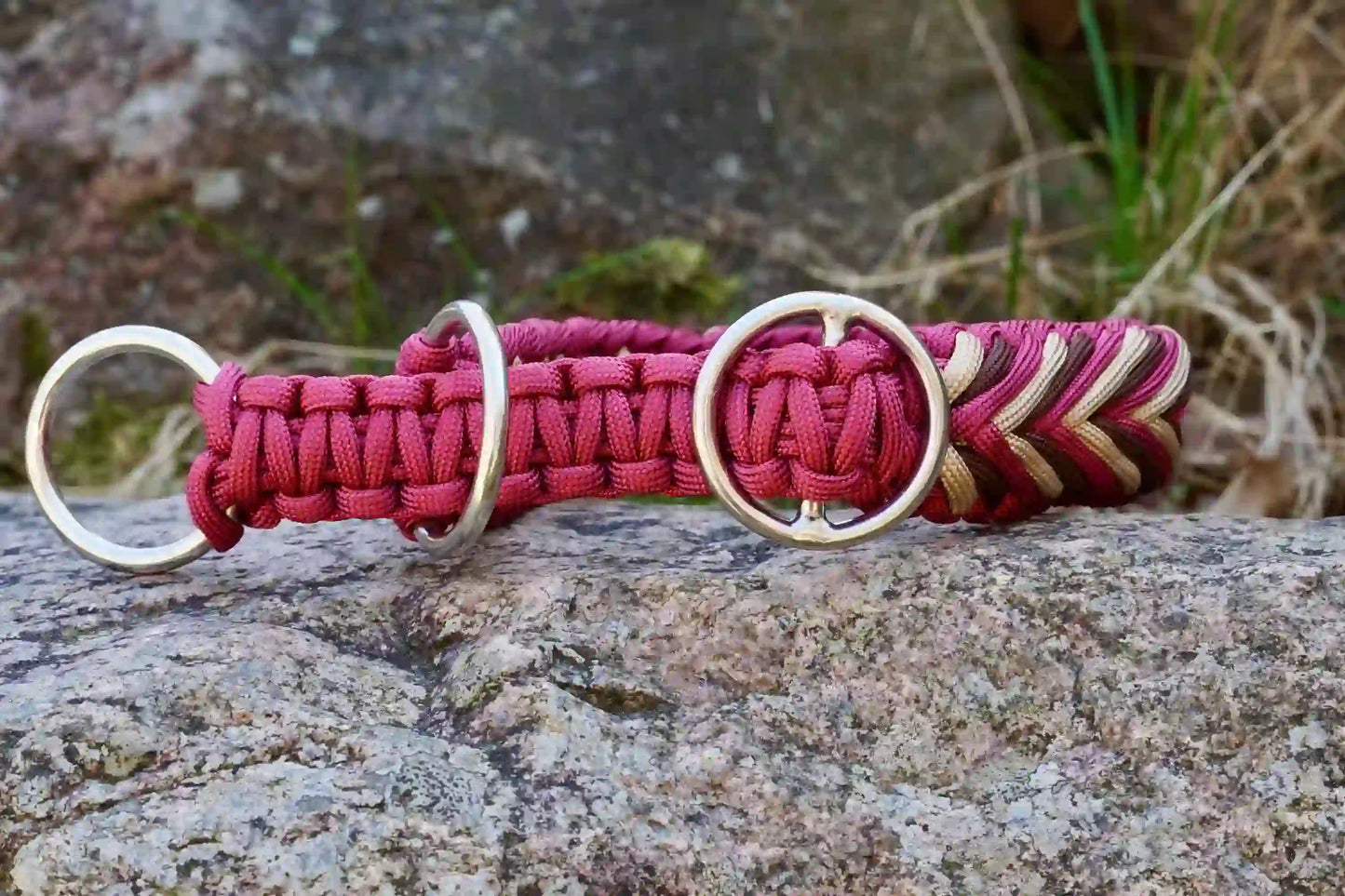 Geflochtenes Hundehalsband in Rot-, Beige- und Brauntönen mit Metallringen auf einem Stein