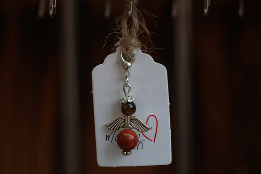 Anhänger in Form eines Schutzengels mit Tigerauge- und roten Jaspisperlen, silberfarbene Flügel, an einem Band befestigt.