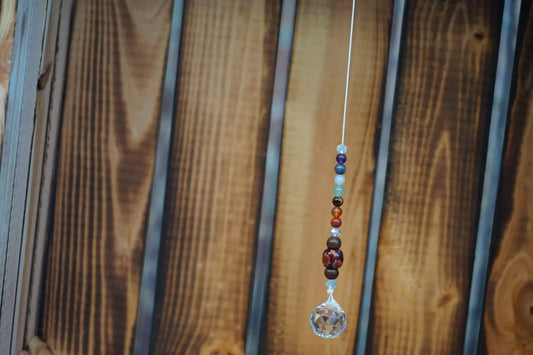Hängender Sonnenfänger mit Edelstein- und Holzperlen, sowie facettiertem Kristallanhänger am unteren Ende mit holzkiste im hintergrund