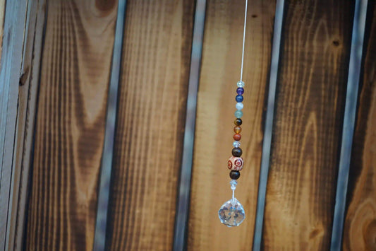Hängender Sonnenfänger mit Edelstein- und Holzperlen, sowie facettiertem Kristallanhänger am unteren Ende mit Holzkiste im Hintergrund
