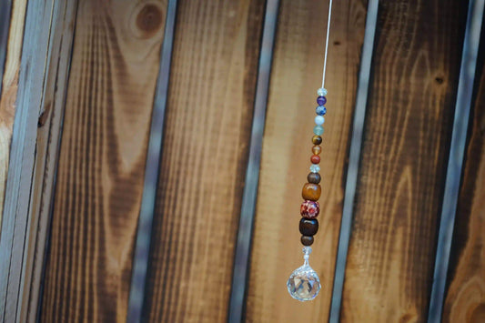 Hängender Sonnenfänger mit Edelstein- und Holzperlen, sowie facettiertem Kristallanhänger am unteren Ende mit holzkiste im hintergrund