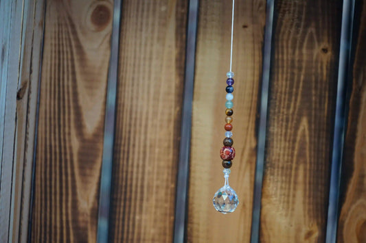 Hängender Sonnenfänger mit Edelstein- und Holzperlen, sowie facettiertem Kristallanhänger am unteren Ende mit holzkiste im hintergrund