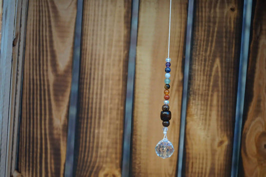 Hängender Sonnenfänger mit Edelstein- und Holzperlen, sowie facettiertem Kristallanhänger am unteren Ende mit holzkiste im hintergrund