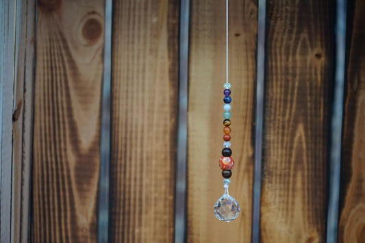 Hängender Sonnenfänger mit Edelstein- und Holzperlen, sowie facettiertem Kristallanhänger am unteren Ende mit holzkiste im hintergrund