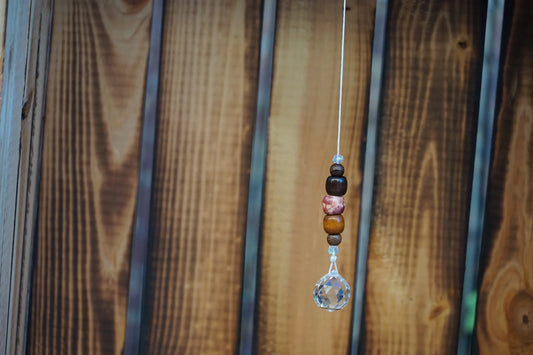Hängender Sonnenfänger mit Holzperlen, sowie facettiertem Kristallanhänger am unteren Ende mit Holzkiste im Hintergrund