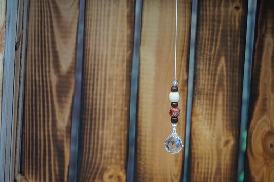 Hängender Sonnenfänger mit Holzperlen, sowie facettiertem Kristallanhänger am unteren Ende mit Holzkiste im Hintergrund