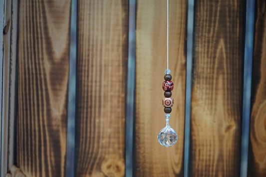 Hängender Sonnenfänger mit Holzperlen, sowie facettiertem Kristallanhänger am unteren Ende mit Holzkiste im Hintergrund