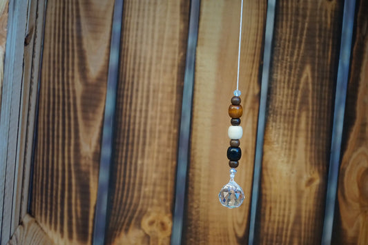 Hängender Sonnenfänger mit Holzperlen, sowie facettiertem Kristallanhänger am unteren Ende mit holzkiste im hintergrund