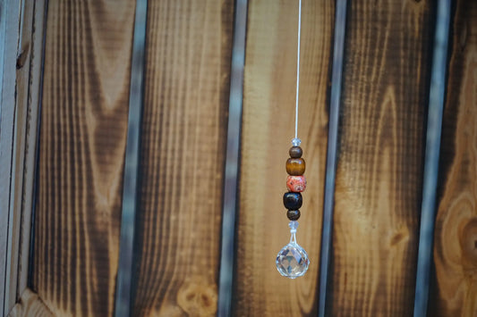 Hängender Sonnenfänger mit Holzperlen, sowie facettiertem Kristallanhänger am unteren Ende mit holzkiste im hintergrund
