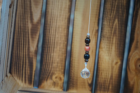Hängender Sonnenfänger mit Holzperlen, sowie facettiertem Kristallanhänger am unteren Ende mit holzkiste im hintergrund