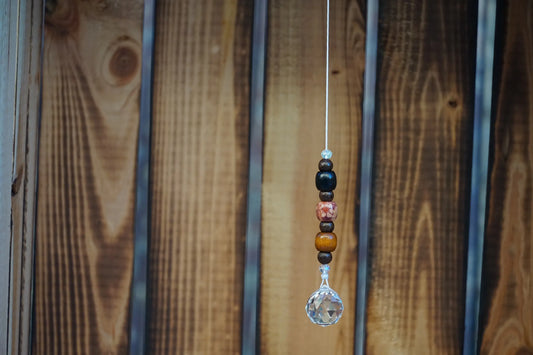 Hängender Sonnenfänger mit Holzperlen, sowie facettiertem Kristallanhänger am unteren Ende mit Holzkiste im Hintergrund