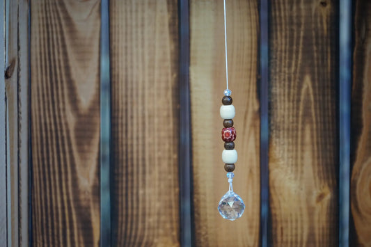 Hängender Sonnenfänger mit Holzperlen, sowie facettiertem Kristallanhänger am unteren Ende mit Holzkiste im hintergrund