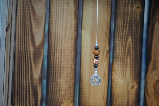 Hängender Sonnenfänger mit Holzperlen, sowie facettiertem Kristallanhänger am unteren Ende mit holzkiste im hintergrund