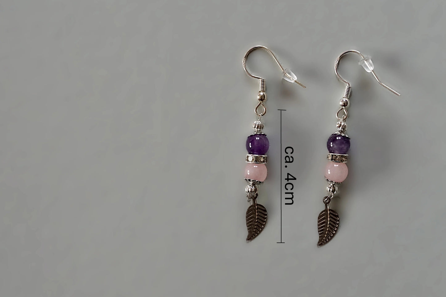 Ohrringe mit silberfarbenen Haken, zwei Edelsteinperlen in Amethyst und Rosenquarz sowie einem silberfarbenen Blattanhänger mit Maßstab