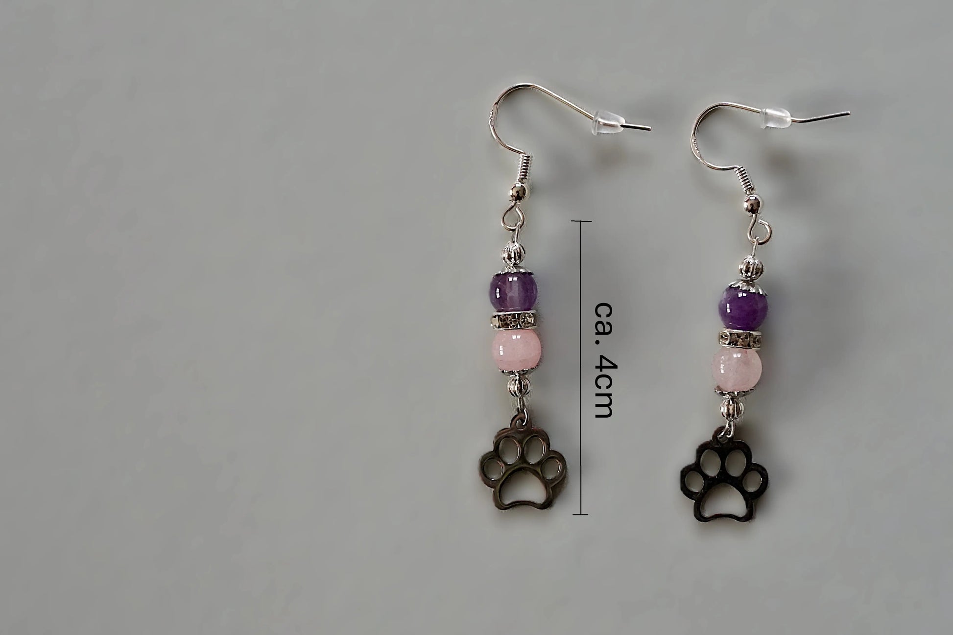Ohrringe mit silberfarbenen Haken, zwei Edelsteinperlen in Amethyst und Rosenquarz sowie einem silberfarbenen Hundepfotenanhänger mit Maßstab