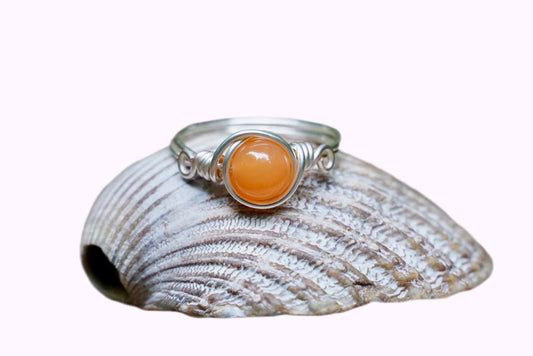 Ring mit einer Karneol Edelsteinperle eingefasst in versilbertem Kupferdraht, platziert auf einer Muschel