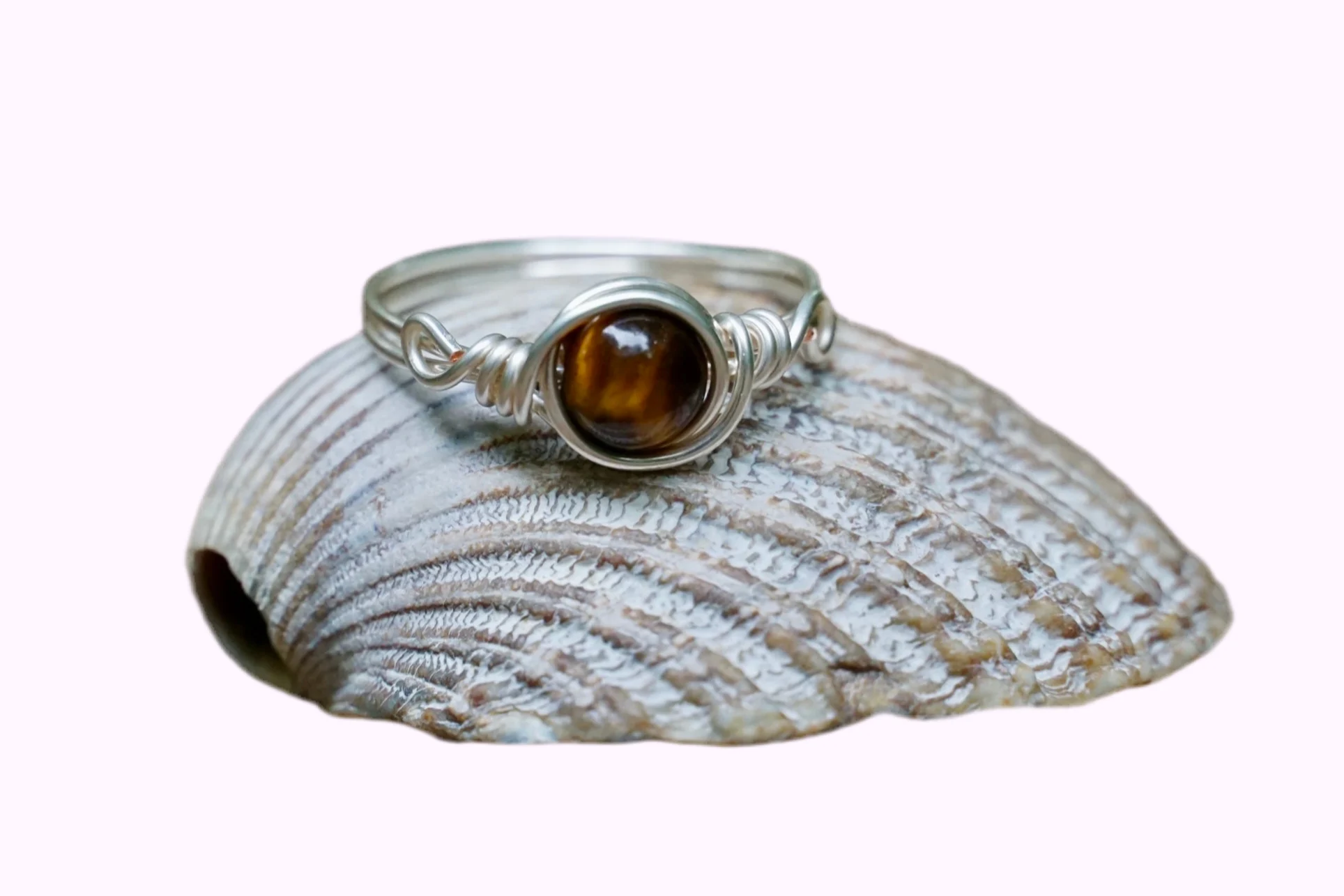 Ring mit versilbertem Kupferdraht und einer Edelstein Tigeraugeperle in der Mitte auf einer Muschel