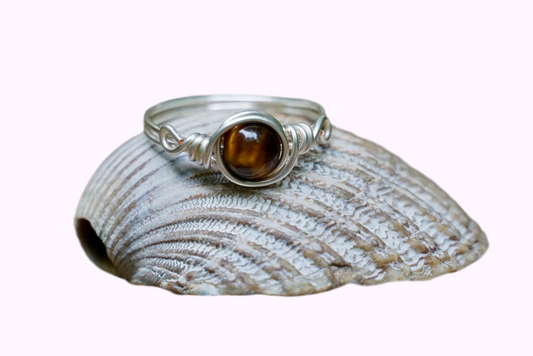 Ring mit versilbertem Kupferdraht und einer Edelstein Tigeraugeperle in der Mitte auf einer Muschel